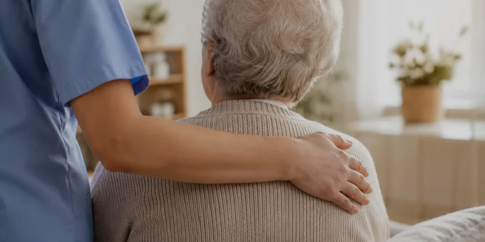 Pflegekraft legt einer Seniorin einfühlsam die Hand auf die Schulter