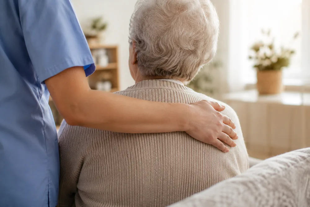 Pflegekraft legt einer Seniorin einfühlsam die Hand auf die Schulter